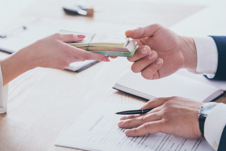 cropped view of woman giving money to manager holding pen near loan agreement